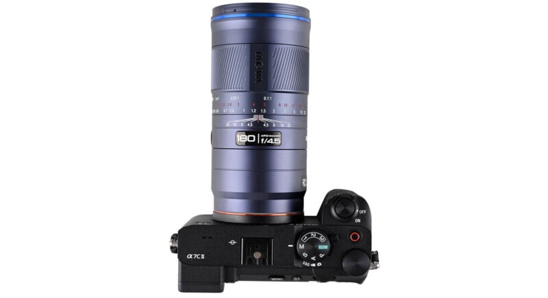 A top view of a black Sony α7C II camera with a large blue and silver Laowa 100mm f/2.8 lens attached, showing detailed controls and dials on the camera body.
