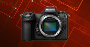 A Nikon Z series mirrorless camera body is displayed against a red, geometric digital background. The camera lens is removed, revealing the image sensor inside.