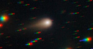 A comet with a bright core and faint tail moves through space, surrounded by colorful, streaked star trails in red, green, and blue on a dark background.