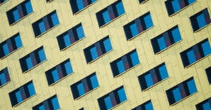 A close-up view of a modern building facade with a diagonal pattern of yellow panels and blue window shades, creating a geometric, repetitive visual effect.