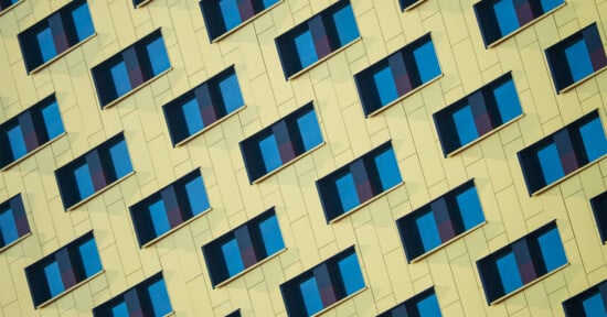 A close-up view of a modern building facade with a diagonal pattern of yellow panels and blue window shades, creating a geometric, repetitive visual effect.