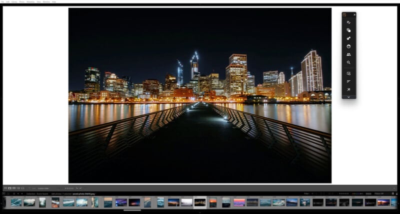 A nighttime cityscape shows tall, brightly lit skyscrapers behind a waterfront. A pier with railings leads toward the city, illuminated by small lights, reflecting on the calm water below. Editing software tools are visible on the screen.