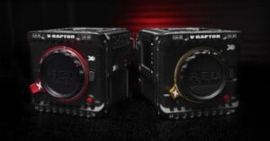 Two black RED V-RAPTOR cinema camera bodies with red and gold accent rings are placed side by side on a dark, glossy surface with a red and black gradient background.