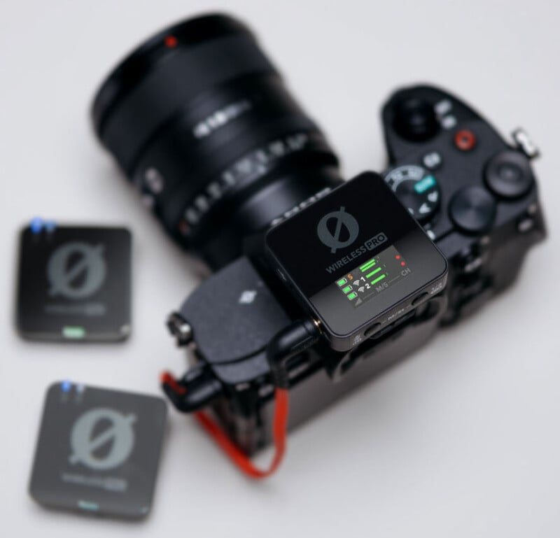 Primer plano de cámara profesional con transmisor profesional inalámbrico conectado a la parte superior. Se colocan dos unidades inalámbricas cercanas sobre una superficie blanca. La cámara tiene una lente grande y controles visibles.