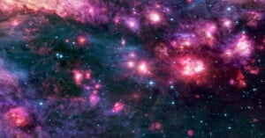 A vibrant image of space shows clusters of bright pink, purple, and blue nebulas and stars scattered across a dark background, illustrating a star-forming region in a distant galaxy.