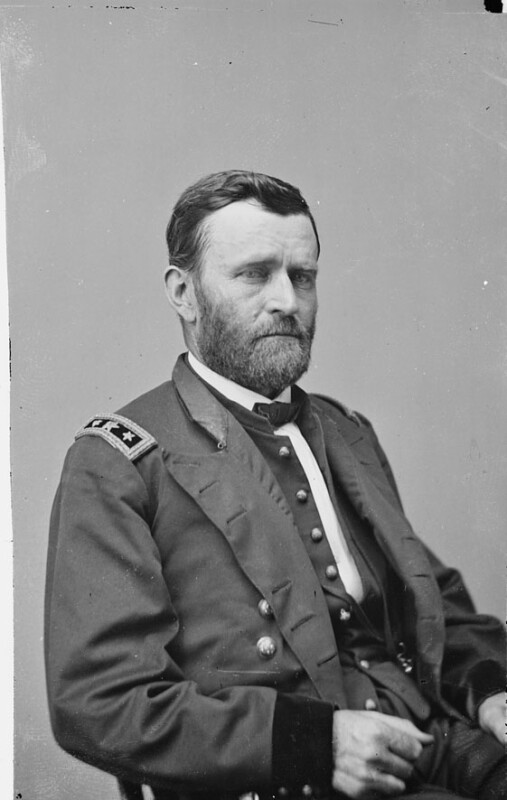 Un hombre barbudo con uniforme militar con botones decorativos y insignias de hombro se encuentra en el lado derecho de la derecha. Su cabello era corto y su expresión era sombría.
