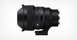 A black camera lens with a wide front element and a tripod collar, shown in a side profile on a white background. Various focus and zoom markings are visible on the lens barrel.