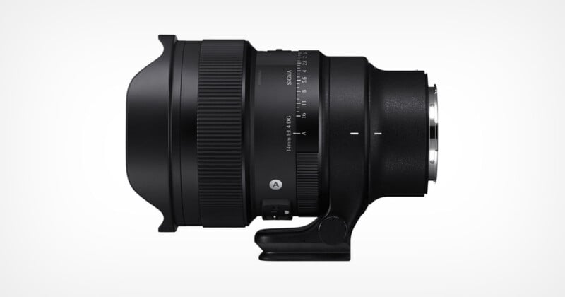 A black camera lens with a wide front element and a tripod collar, shown in a side profile on a white background. Various focus and zoom markings are visible on the lens barrel.