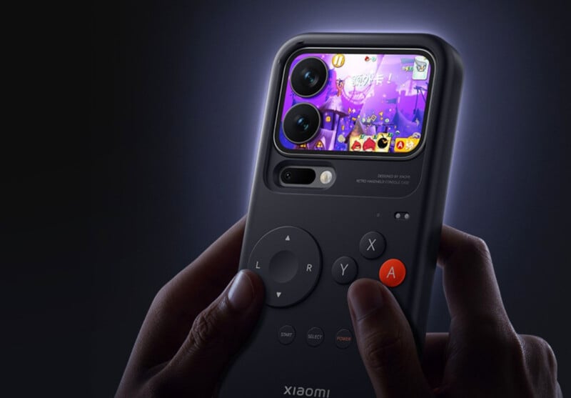 A person holds a Xiaomi device resembling a retro handheld gaming console with a screen displaying a colorful game and two camera lenses above the screen. The console has gaming buttons and a directional pad.