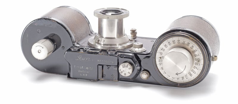 Top view of a vintage Leica camera, showing its metal body, winding knobs, engraved dials, and visible lens mount, with "Ernst Leitz Wetzlar" and model details inscribed on the surface.