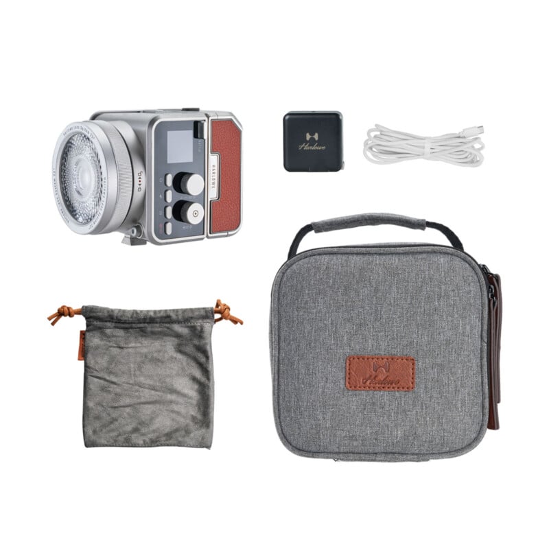 Un flash de cámara con ribete marrón, un dispositivo negro, un cable USB blanco, una bolsa gris con cordón y una maleta gris con cremallera y parches marrones, todo ello sobre un fondo blanco.