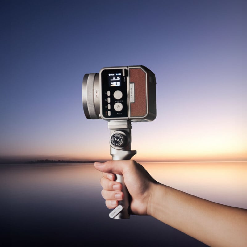 Una mano sostiene una cámara retro en un cardán con un lago tranquilo y un colorido cielo al atardecer en el fondo.
