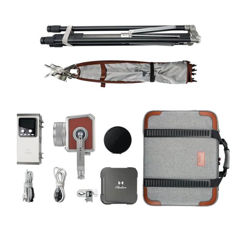 Plano de equipo de cámara que incluye trípode, cámara, maleta, cables, accesorios de cámara, bolsas blandas y pequeños parlantes negros redondos, todo cuidadosamente dispuesto sobre fondo blanco.