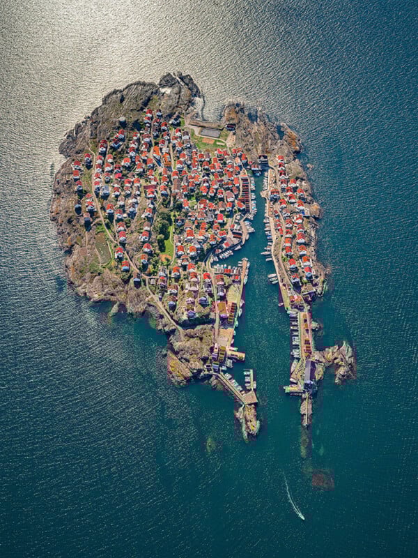 Vista aérea de una pequeña isla rocosa salpicada de casas muy juntas con techos rojos y rodeada de agua azul; muelles y barcos se alinean en el borde de la isla.