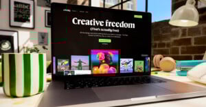 A laptop on a desk displays the Affinity website with the message "Creative freedom (That's actually free)" on the screen. The desk has a green-striped mug, headphones, and various art supplies.