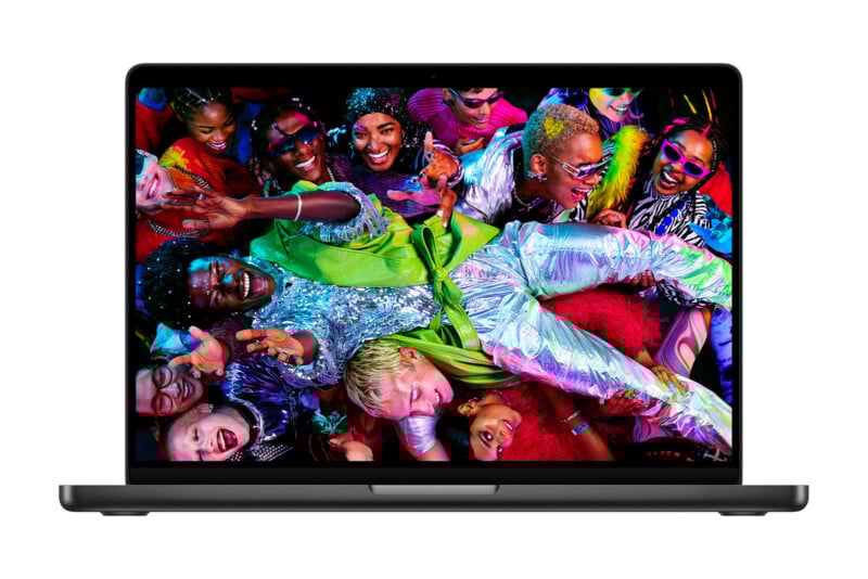 A MacBook laptop displays a vibrant image of a diverse group of people in colorful, sparkling outfits joyfully celebrating and laughing together.