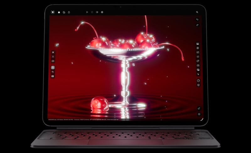 A laptop displays a digital image of bright red cherries in a shiny glass dish, with a deep red background and rippling reflections beneath the dish. The screen features various editing tool icons.