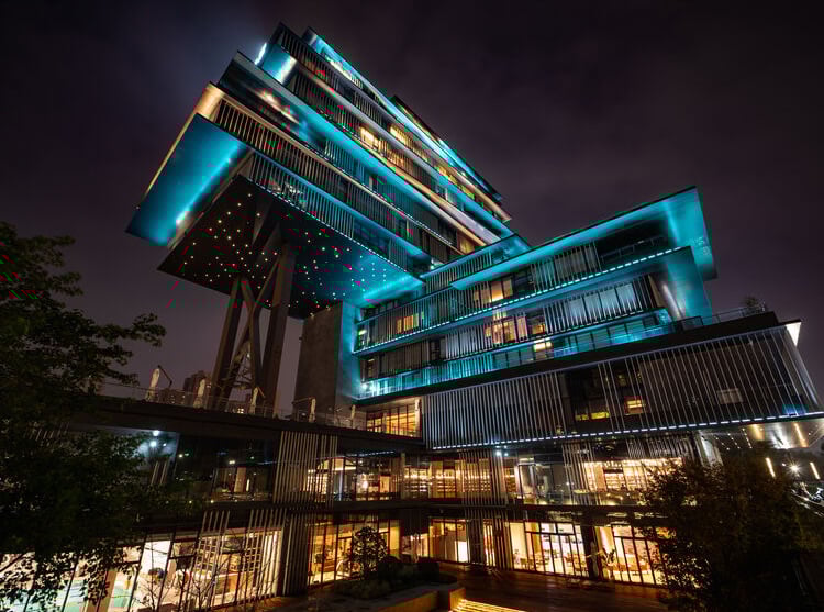 A modern, multi-level building with futuristic, angular design is illuminated by blue and orange lights against a night sky, creating a dramatic and striking appearance.