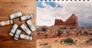 Seven film canisters on a wooden surface next to a scenic photo of a rocky desert landscape with a large rock formation, sparse vegetation, and a cloudy sky. The photo has a film strip edge at the top.