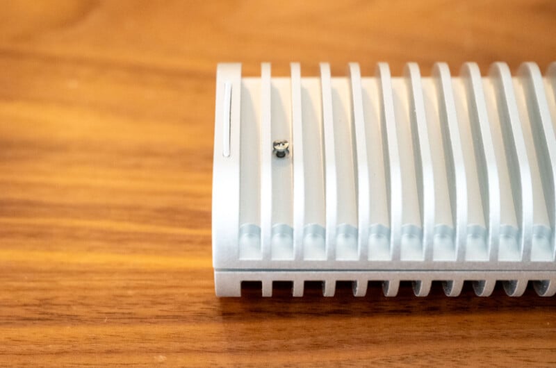 A small insect sits on a white, ribbed electronic device placed on a wooden surface, with the focus on the device and insect, and the background blurred.