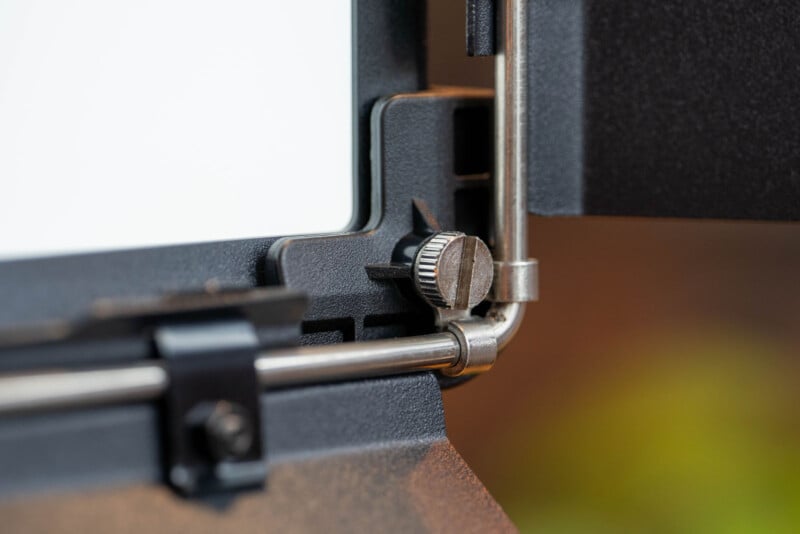 Close-up of a metal screw adjustment knob on a black and silver frame, possibly part of a camera, light fixture, or mechanical equipment, with blurred background.