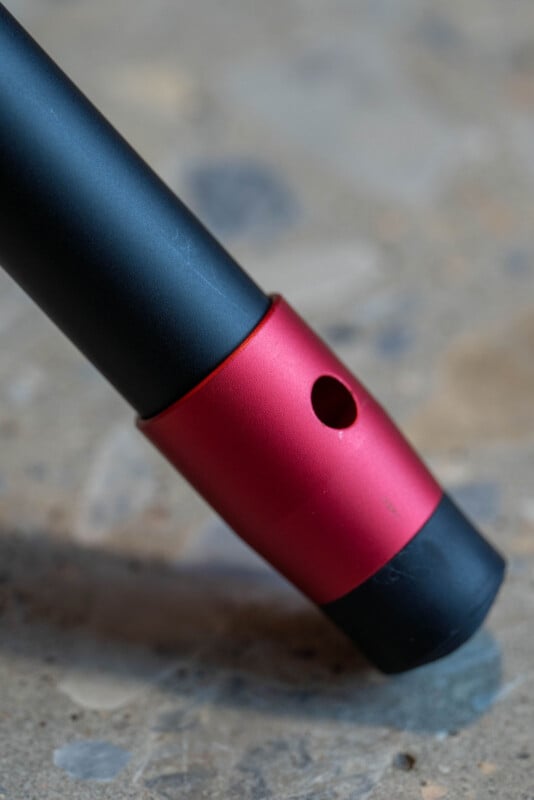 Close-up of a black and red cylindrical object with a hole in the red section, resting on a textured, stone-like surface.