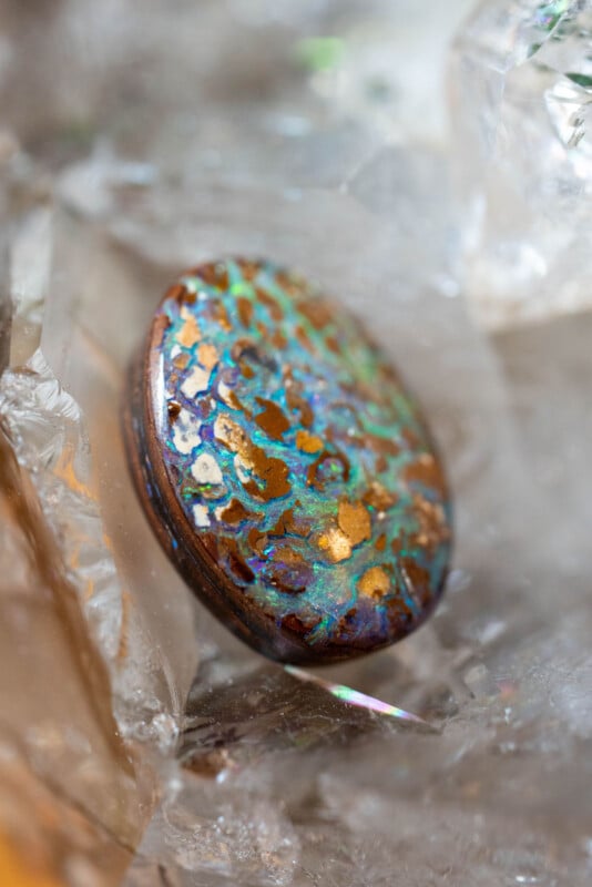 A close-up of a polished gemstone with an intricate mix of turquoise, gold, and brown patterns, surrounded by clear, faceted crystal surfaces.