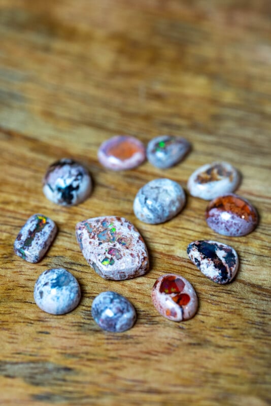 A collection of polished opal stones with various patterns and colors, including specks of green, blue, and red, displayed on a wooden surface.