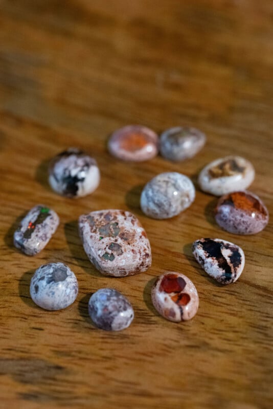 A group of polished, oval and round stones with various patterns and colors, including white, brown, orange, and black, displayed on a wooden surface.
