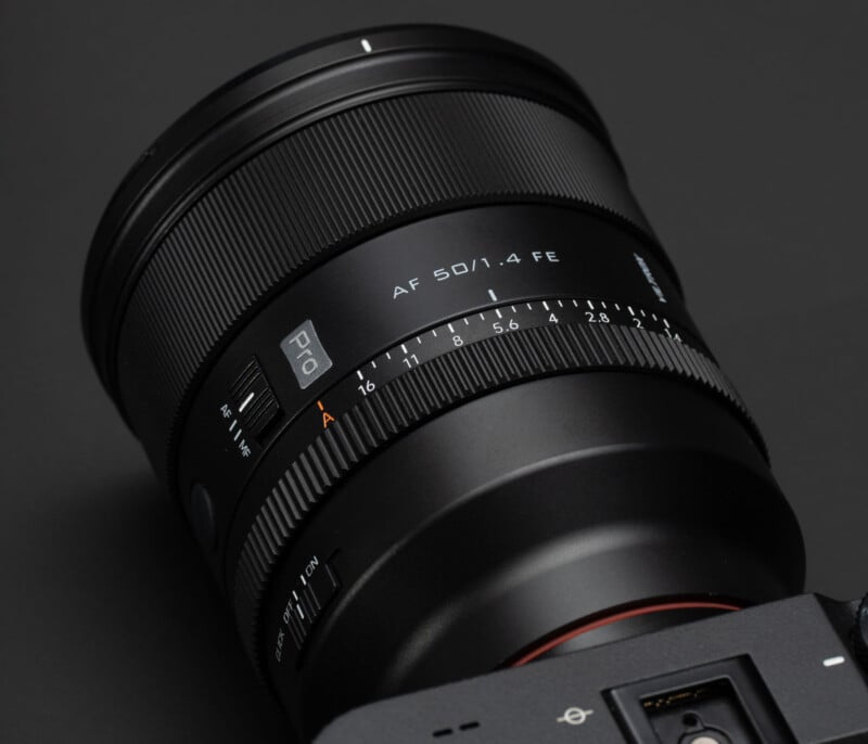 Close-up of a black 50mm f/1.4 camera lens attached to a camera body, showing detailed focus and aperture markings, with a matte finish and textured grip on a dark background.