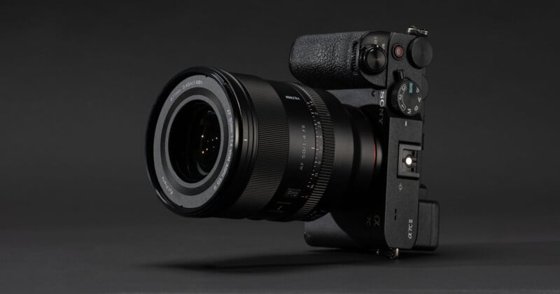 A black Sony mirrorless digital camera with a large detachable lens, displayed against a dark, seamless background. The camera is angled slightly to show its controls and textured grip.