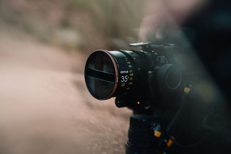 Close-up of a professional camera with a 35mm lens outdoors, showing detailed focus and aperture markings on the lens barrel, with a blurred natural background.