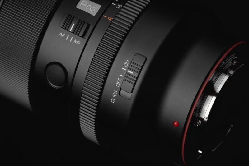 Close-up of a black camera lens showing buttons and switches for autofocus/manual focus, a ring with textured grip, and a “CLICK OFF/ON” switch, against a dark background.
