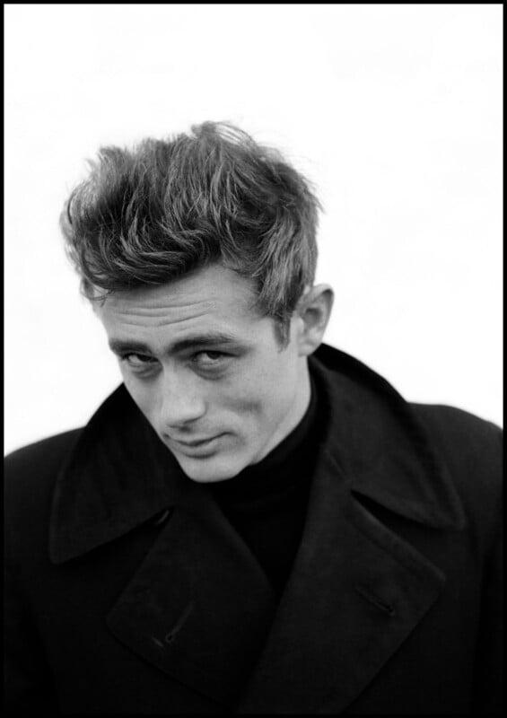 Black-and-white portrait of a man with tousled hair, wearing a dark coat and turtleneck, looking slightly downward with a serious, intense expression against a plain background.
