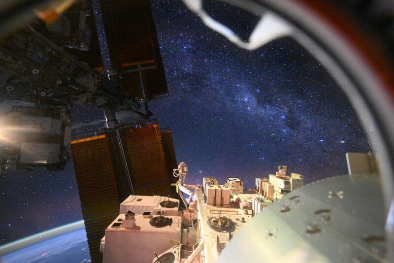 Vista de la Estación Espacial Internacional que muestra paneles solares, equipos y el horizonte de la Tierra con un cielo lleno de estrellas y la Vía Láctea al fondo.