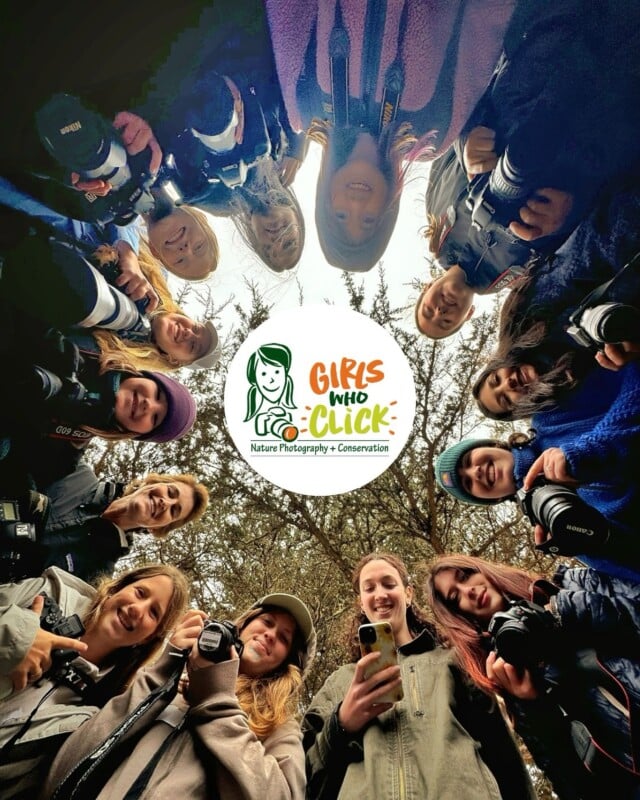A group of young women holding cameras stand in a circle outdoors, looking down at the camera. In the center, a "Girls Who Click" logo with the tagline "Nature Photography + Conservation" is displayed.