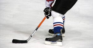 A hockey player on ice in black skates and blue-and-white socks controls a puck with a black stick, preparing to make a move during a game.