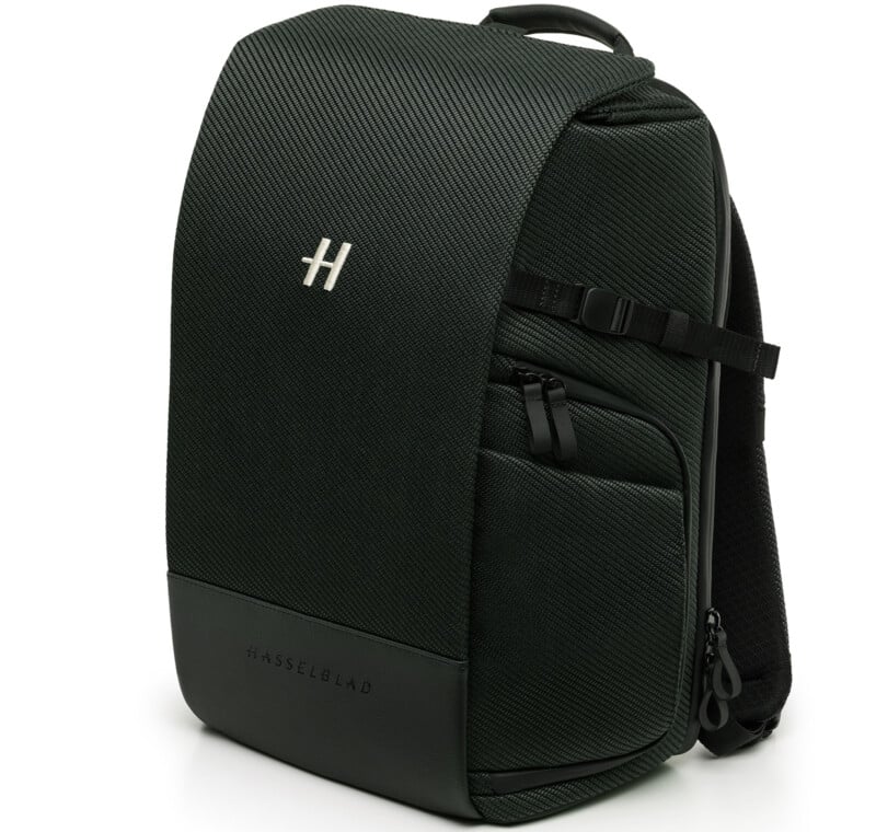A black Hasselblad-branded backpack with a textured surface, front pocket, side zipper, adjustable strap, and a top handle, photographed against a white background.