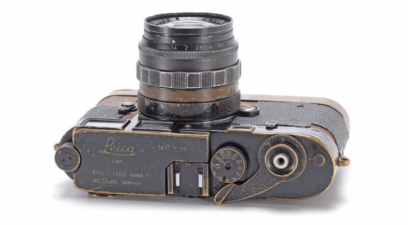 A vintage black Leica MP camera with visible wear, featuring a textured body, metal dials, and a prominent lens. The engraved “Leica” logo and “ERNST LEITZ GMBH WETZLAR GERMANY” are shown on the top plate.
