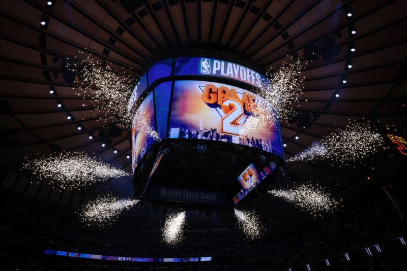 A large scoreboard in an arena displays "PLAYOFFS GAME 2" with fireworks and bright sparks shooting out around it, under the dome ceiling of Madison Square Garden.
