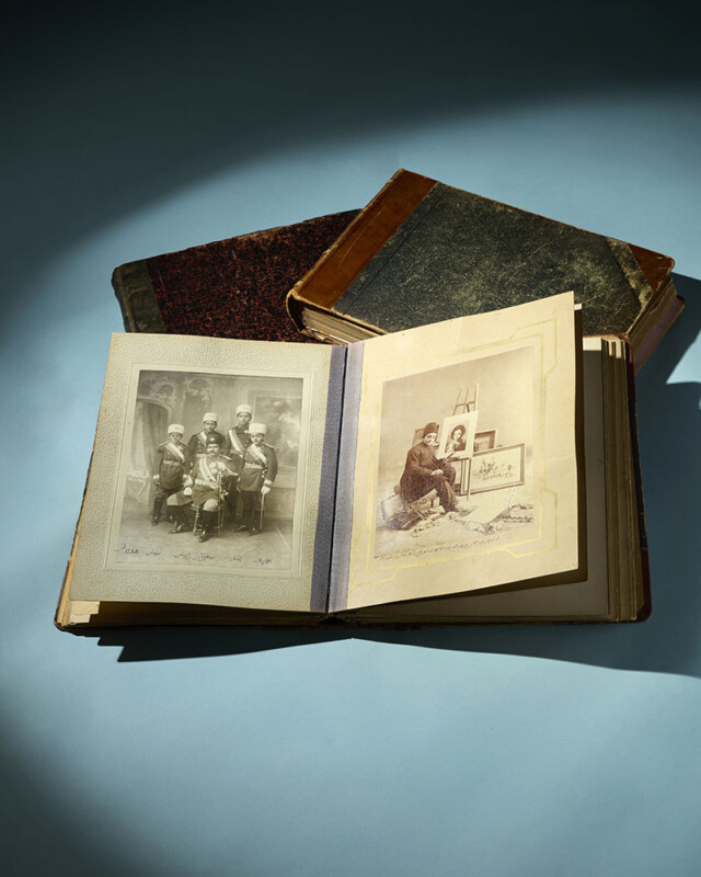 Un álbum de fotos antiguo abierto que muestra un retrato en blanco y negro junto a dos libros antiguos cerrados, todo sobre un fondo azul claro con una iluminación suave.