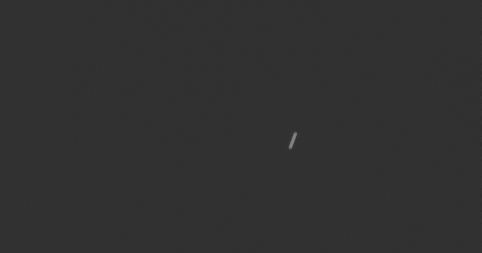 A small, thin white line appears slightly right of center on a dark grey background, with no other visible objects or details.