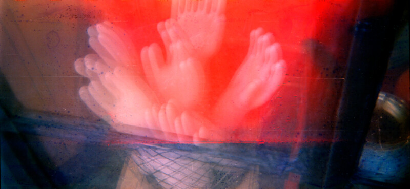 A cluster of white rubber gloves appears layered and blurred, creating a ghostly effect against a background of vivid red and blue hues. The scene is abstract, with soft, overlapping shapes and a basket visible below the gloves.