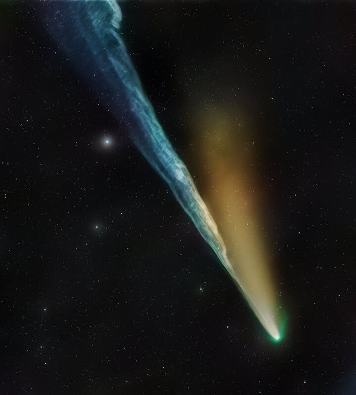 A bright comet with a glowing green head and long blue and orange tails streaks across a star-filled, dark night sky.