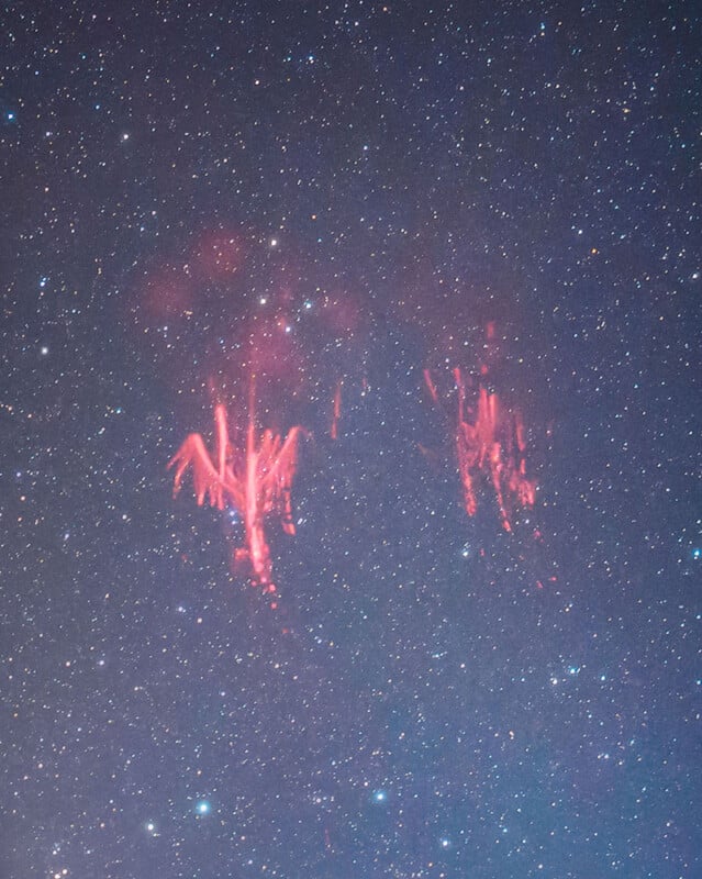 A star-filled night sky features bright, reddish, tentacle-like lightning formations, known as red sprites, illuminating the upper atmosphere.