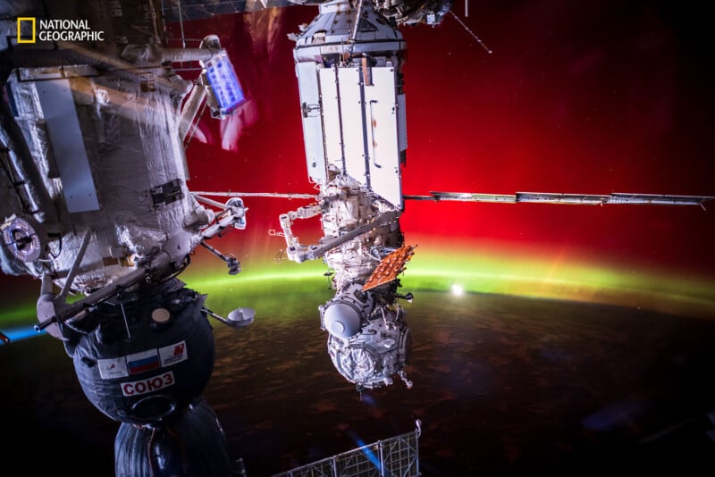 Vista de una nave espacial acoplada a la Estación Espacial Internacional, con auroras verdes y rojas visibles en el horizonte de la Tierra al fondo. El indicador National Geographic está en la esquina superior izquierda.