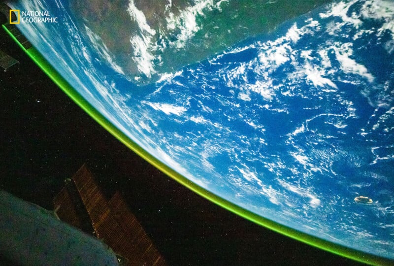 Al mirar la Tierra desde el espacio, se pueden ver océanos azules, nubes blancas y partes de continentes, y a lo largo del borde se puede ver una delgada línea verde de atmósfera. El indicador National Geographic aparece en la esquina superior izquierda.