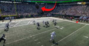 A football is in mid-air near the end zone during an NFL game, with several players looking up to catch it. The stands are full of spectators, and the Fox NFL logo appears in the top right corner.