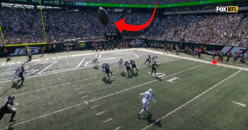 A football is in mid-air near the end zone during an NFL game, with several players looking up to catch it. The stands are full of spectators, and the Fox NFL logo appears in the top right corner.
