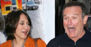 A woman and a man stand close together, both with surprised and animated facial expressions. The background features a movie poster with cars and bright colors.